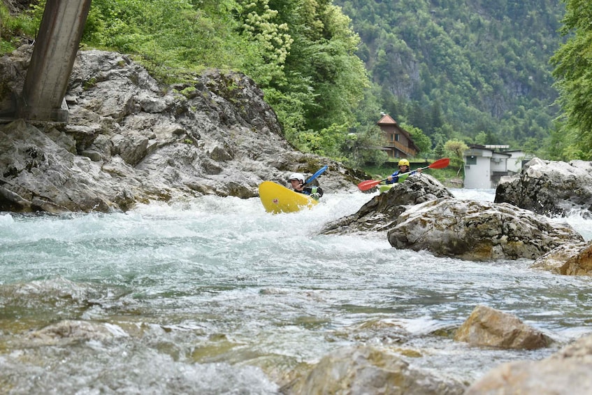 Two kayakers navigating a river with rapids, surrounded by rocky terrain and lush greenery. 5