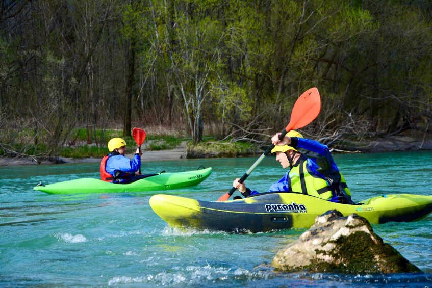 Two kayakers in bright-colored kayaks on a river with trees in the background. 1