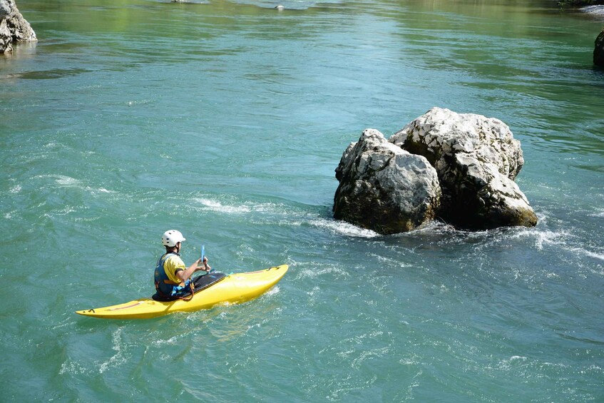 A person kayaking on a river with a large rock formation in the water. 4