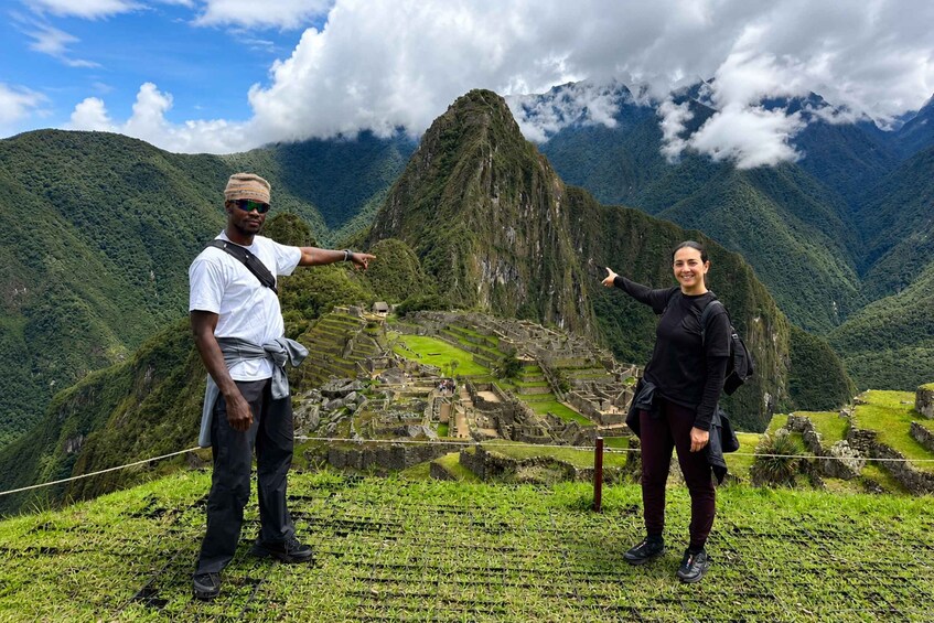 Two people standing on a grassy area with a view of Machu Picchu in the background. 2