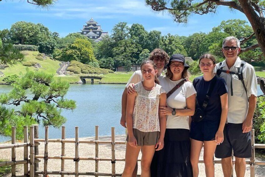 A group of people standing by a lake with a traditional Japanese building in the background. 1