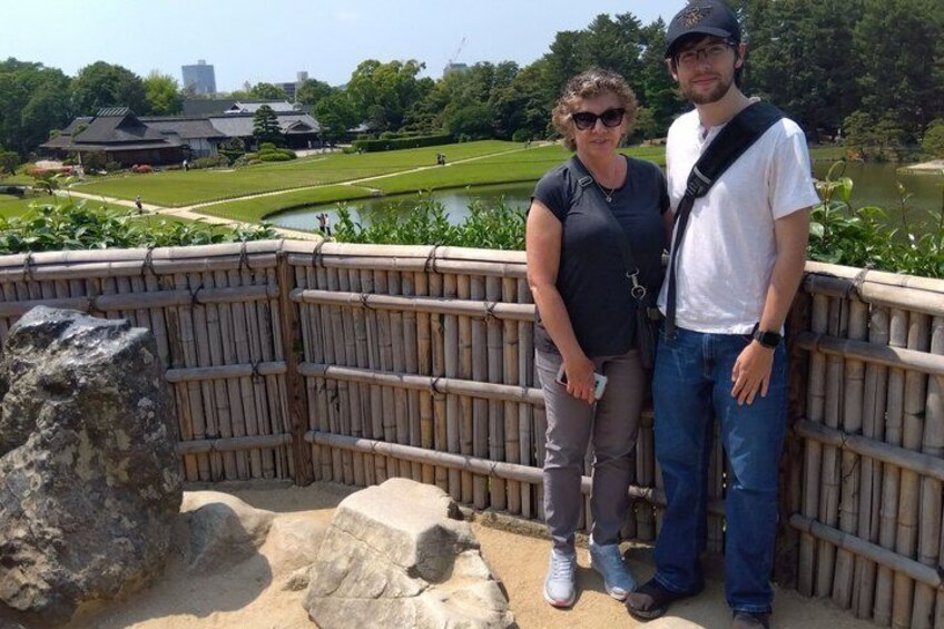 A couple standing on a bamboo fence overlooking a lake with a traditional building in the background. 4