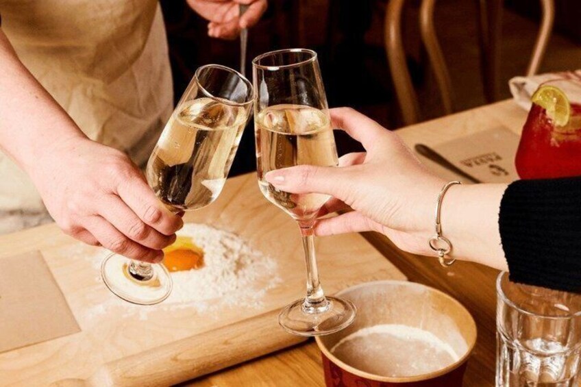 Two people toasting with champagne glasses, a wooden table, a red drink with a lemon garnish, and a bowl of flour. 2