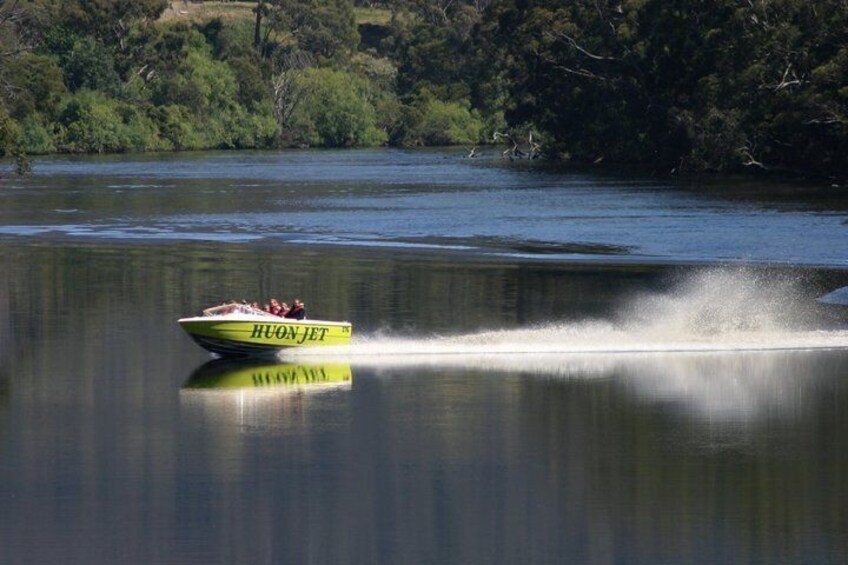 A speedboat named HUONJET moving across a calm lake, creating a wake behind it. 3