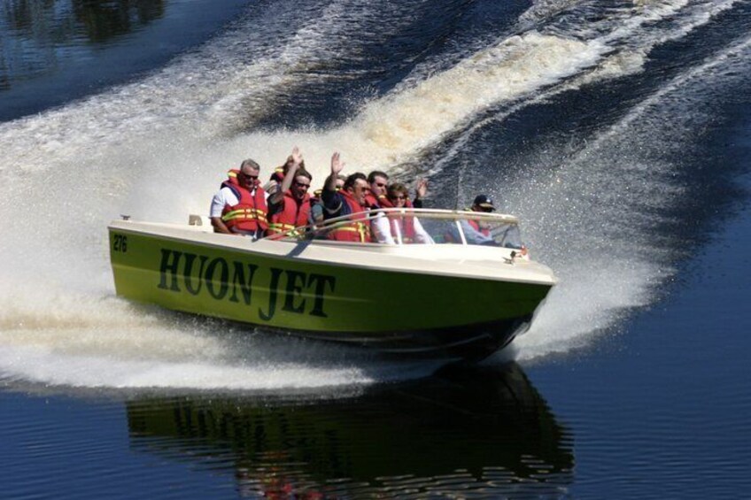 A green boat named HUON JET moving swiftly on water. 1