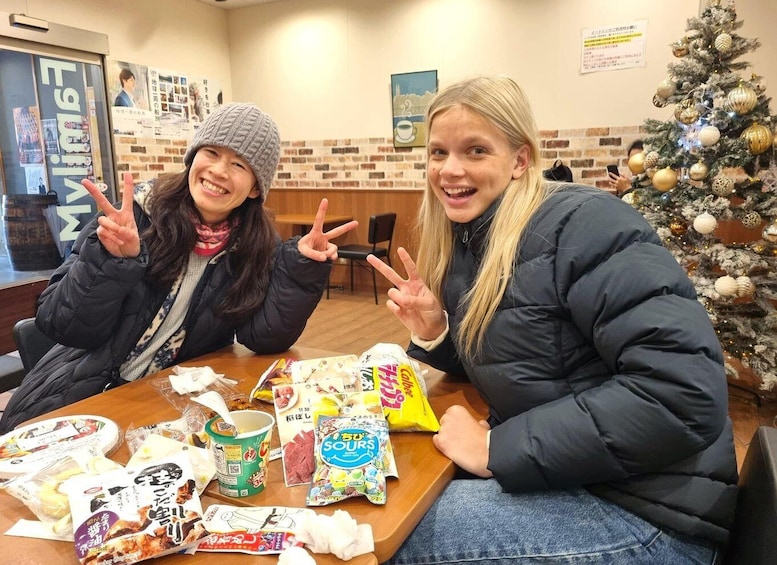 Two people sitting at a table with various food items and a Christmas tree in the background. 1