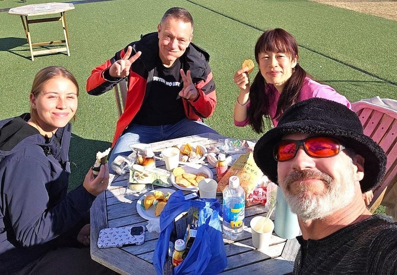 A group of people sitting at a table outdoors with food and drinks. 4