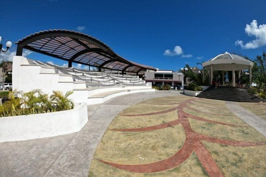A modern architectural structure with a curved roof, a central open space with a star-shaped design, and a gazebo-like building in the background. 3