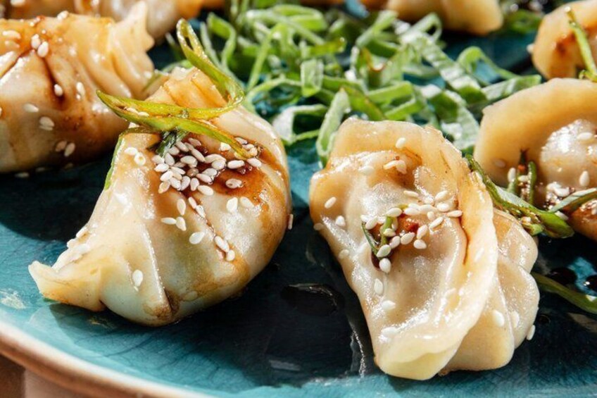 Dumplings garnished with sesame seeds and green herbs on a blue plate. 2