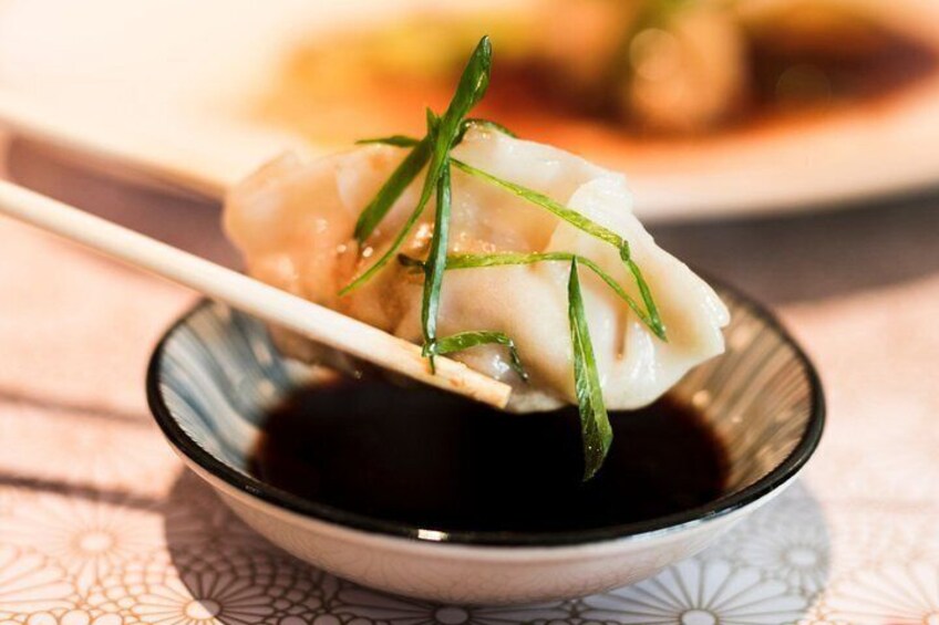A bowl of dumplings with a dipping sauce and a pair of chopsticks. 5