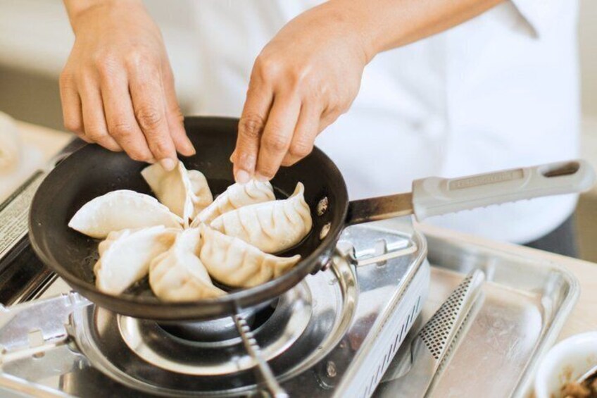 Hands placing dumplings into a pan on a stove. 1