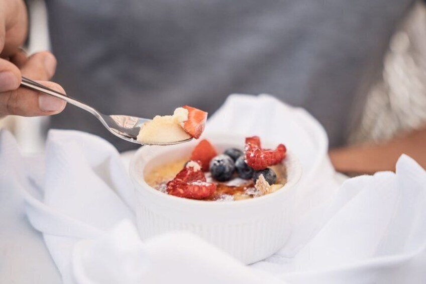 A dessert in a white bowl with strawberries, blueberries, and raspberries on top. 4