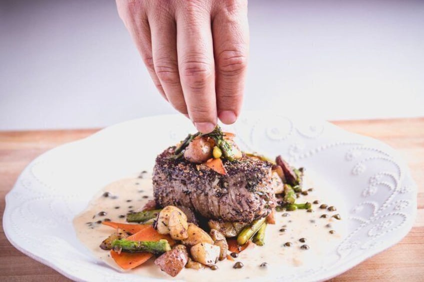 A hand placing a garnish on a steak with vegetables on a plate. 1