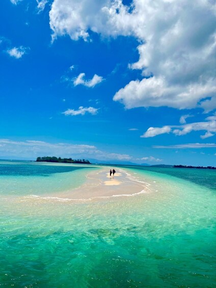 A beach with clear turquoise water, a sandy shore, and two people walking towards the water. 1