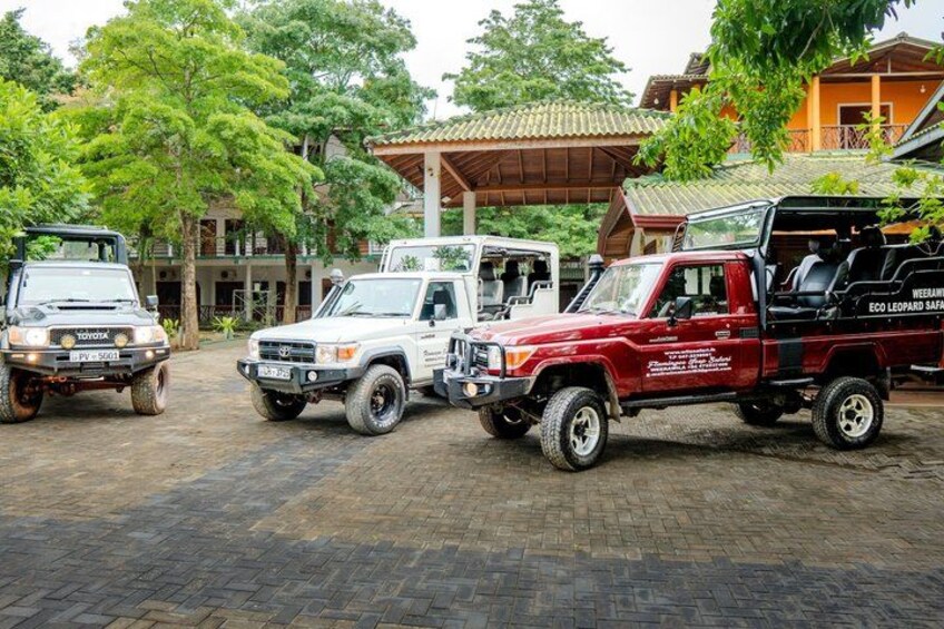 Three off-road vehicles parked on a paved area with trees and buildings in the background. 5