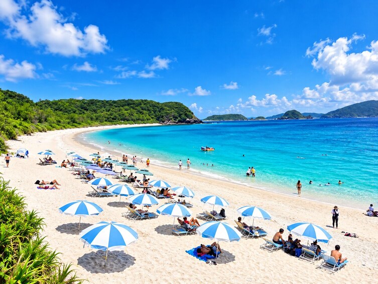 A beach with clear turquoise water, people sunbathing under blue and white striped umbrellas, and lush green hills in the background. 1