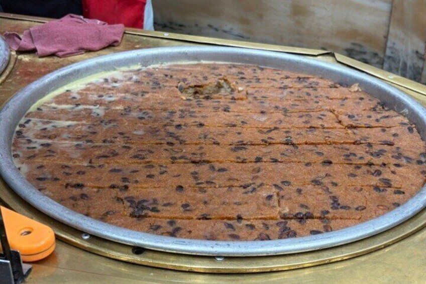 A large metal tray with a baked dish, possibly a pie or cake, with a golden-brown crust and dark spots, likely chocolate chips or raisins. 3