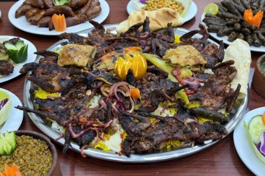 A large platter of grilled meats and vegetables, surrounded by various side dishes and bread. 5
