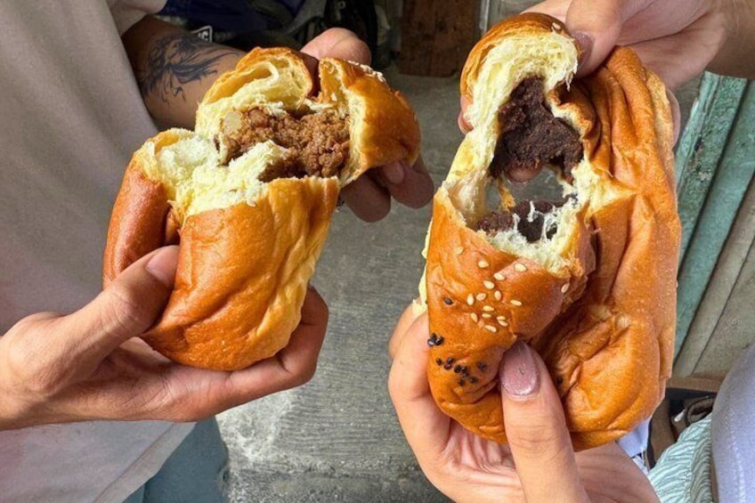 Two hands holding a stuffed bread roll with sesame seeds. 3