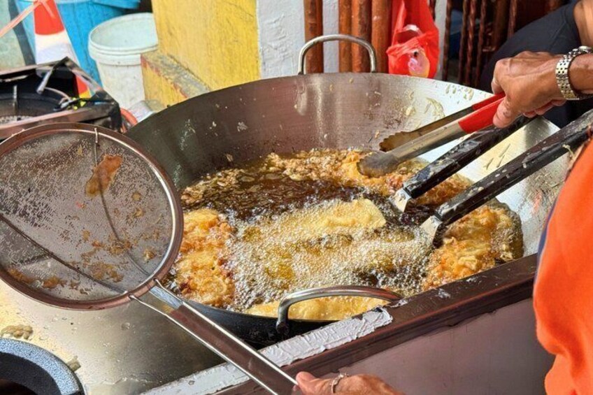 A large frying pan with food being deep-fried, a strainer, and a person wearing an orange garment. 2