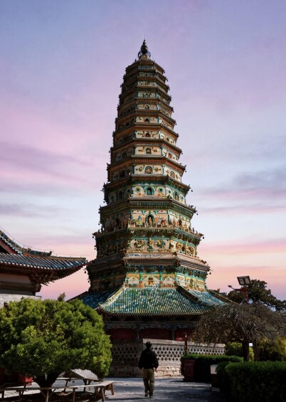 A multi-tiered pagoda with intricate designs, a person walking in front, and traditional architecture. 5
