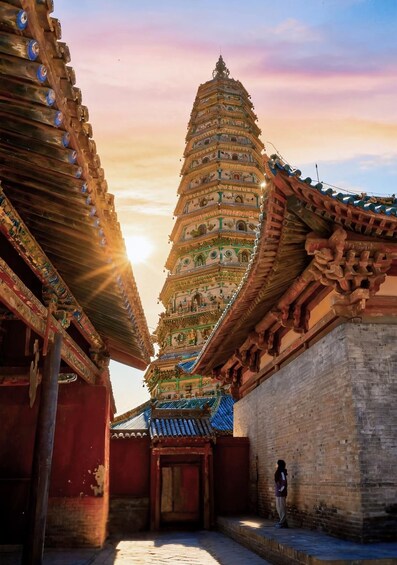 A traditional multi-tiered temple with intricate carvings and a person standing in the foreground. 1