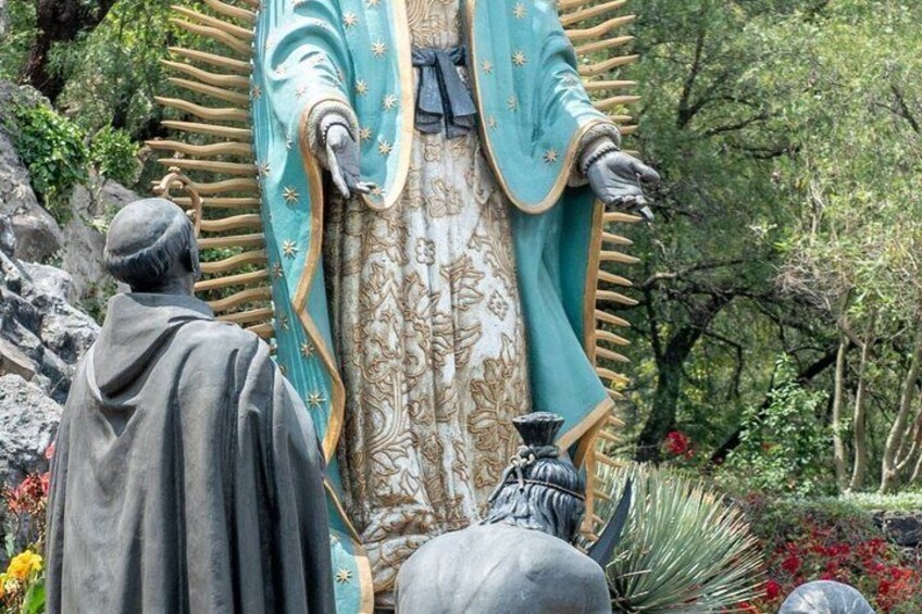A statue of a figure in a blue robe with gold trim, standing in a garden with trees and flowers. 3