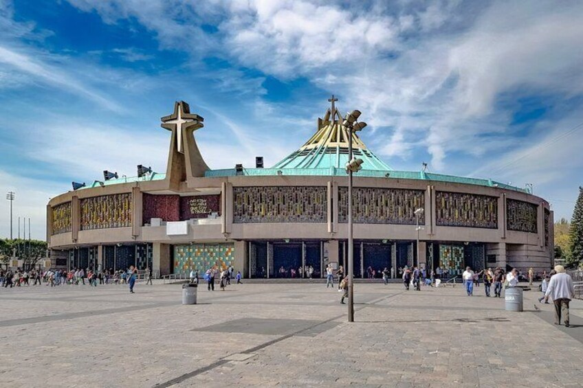A large circular building with a cross on top, surrounded by a plaza with people. 1