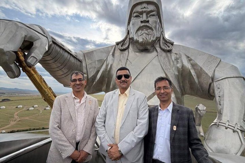 Three men standing in front of a large statue with a landscape in the background. 5