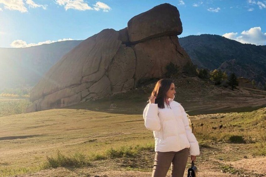 A person standing in a grassy field with a large rock formation in the background. 3