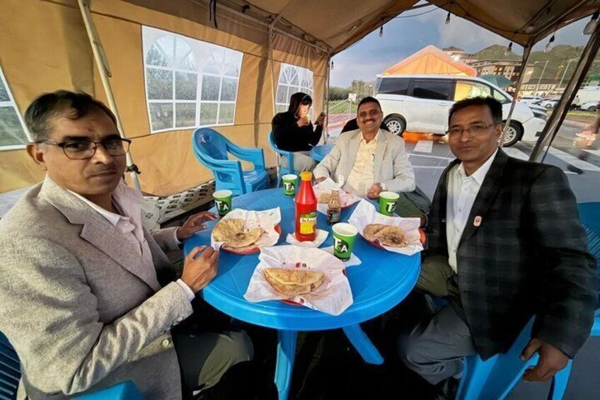 Three people sitting at a blue table with food and drinks, under a tent. 4