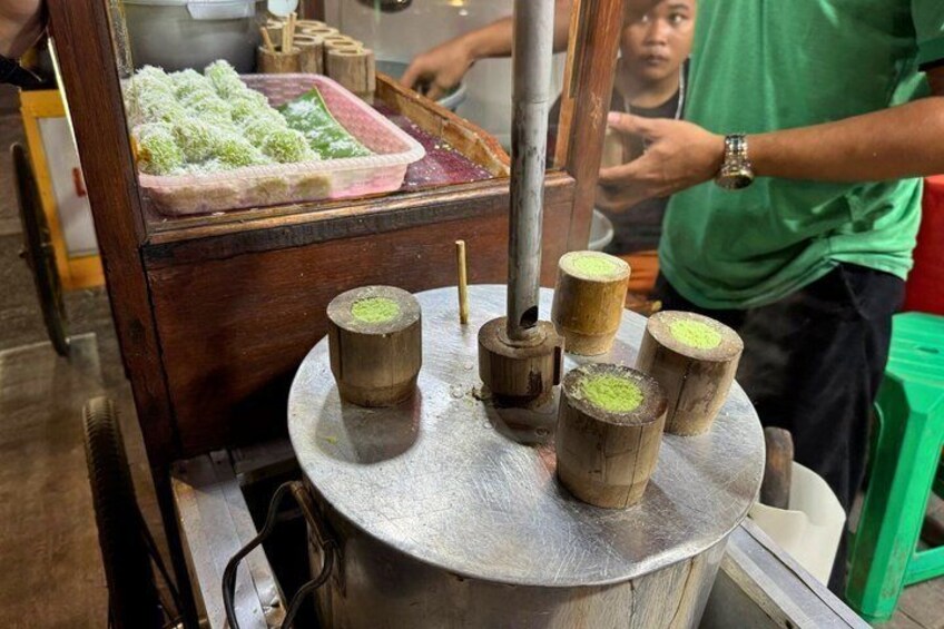 A food stall with a traditional wooden structure, a metal cooking surface, and a tray of food. 4