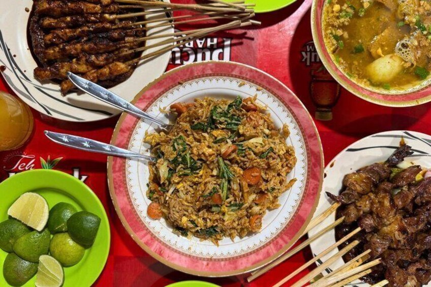 A table with various dishes including grilled meat, rice, and a soup. 1