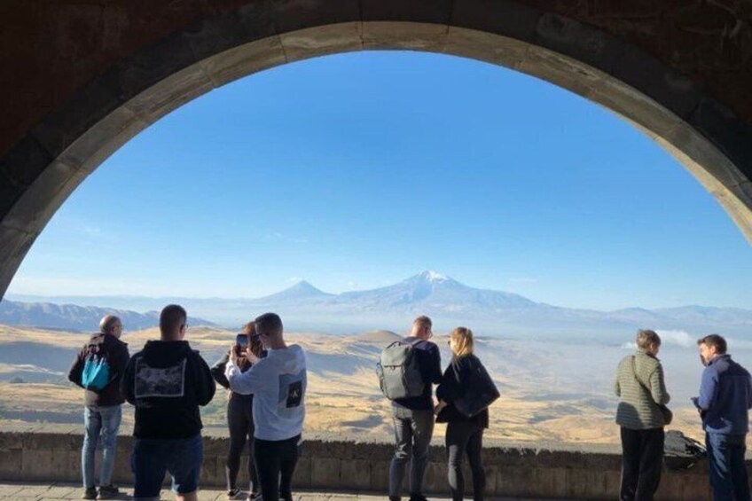 A group of people standing in an archway overlooking a mountainous landscape with a prominent peak. 2