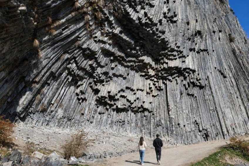 A large rock formation with a distinct layered pattern, a clear sky, and a dirt path. 3