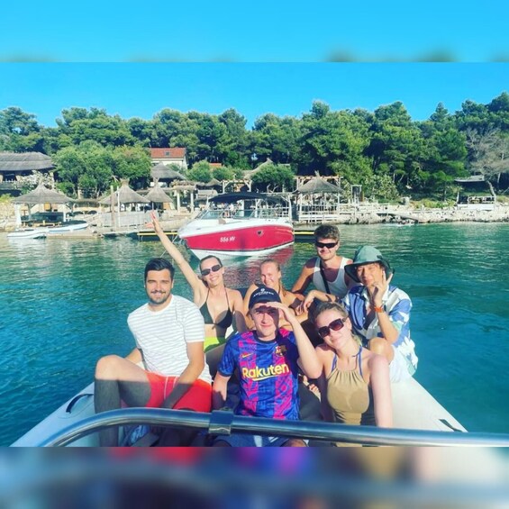 A group of people on a boat with a red and white vessel in the background, surrounded by a coastal landscape with buildings and trees. 1