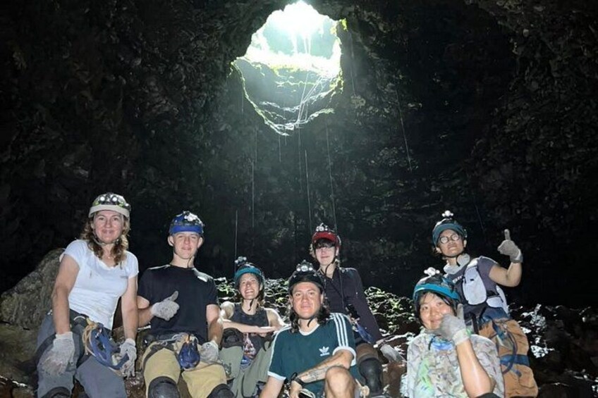 A group of people sitting in a cave with a large opening at the top. 3