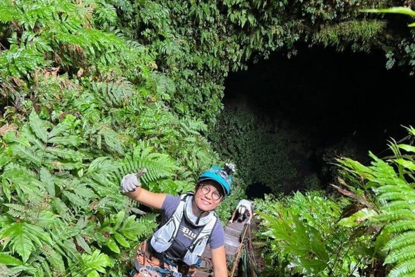 A person hiking in a dense forest with ferns and a cave entrance. 5