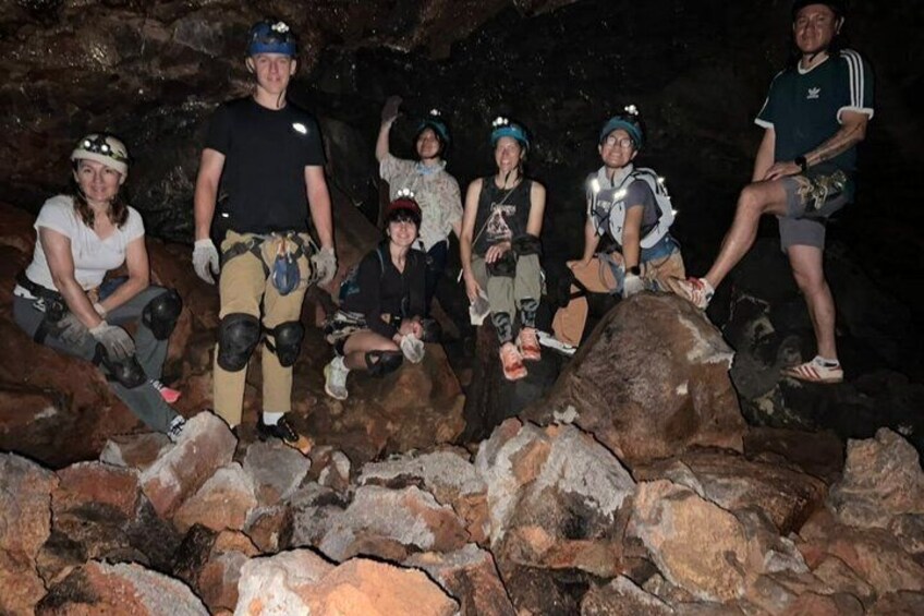 A group of people in helmets and climbing gear sitting on rocks in a cave. 4