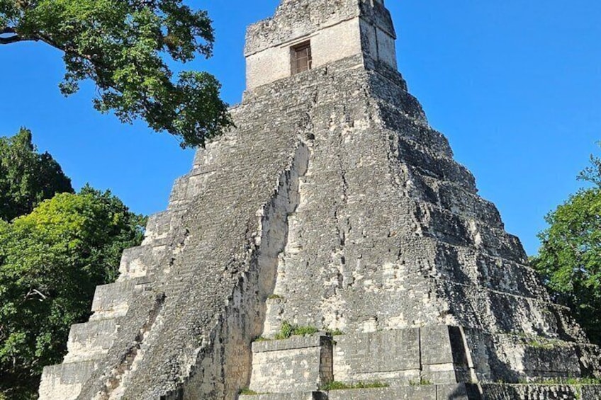 A large ancient pyramid with a smaller structure on top, surrounded by trees. 3