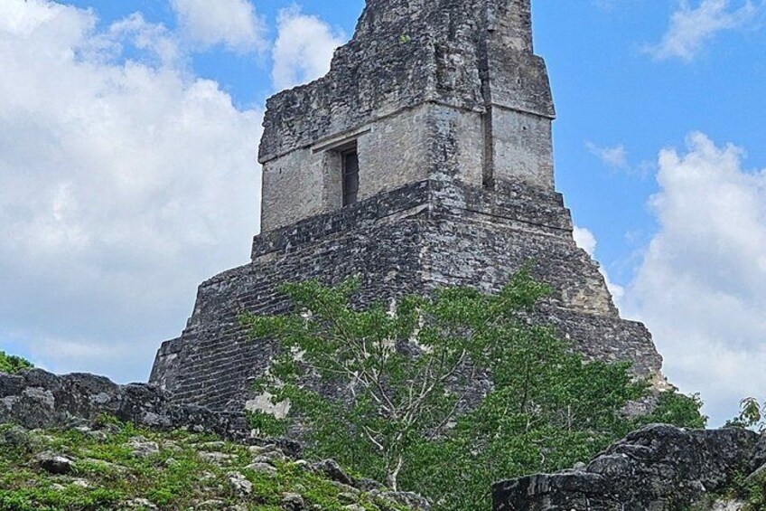 A large ancient pyramid with a small window, surrounded by rocky terrain and sparse vegetation. 1
