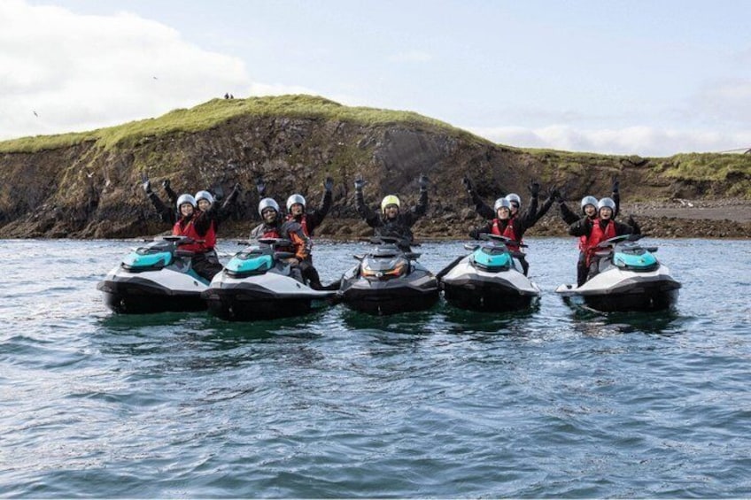 Four people on jet skis in a body of water with a rocky coastline in the background. 1