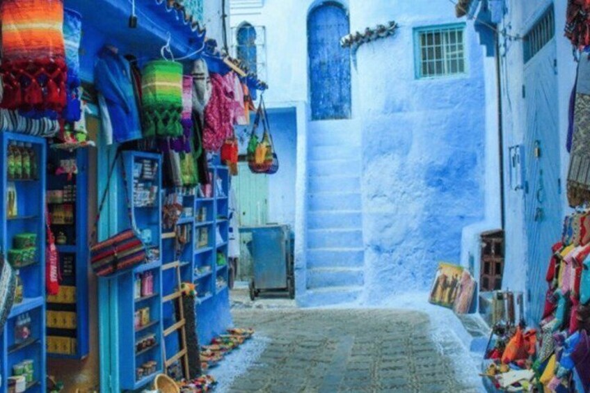 A narrow alley with blue-painted buildings, colorful hanging items, and a staircase leading up. 5