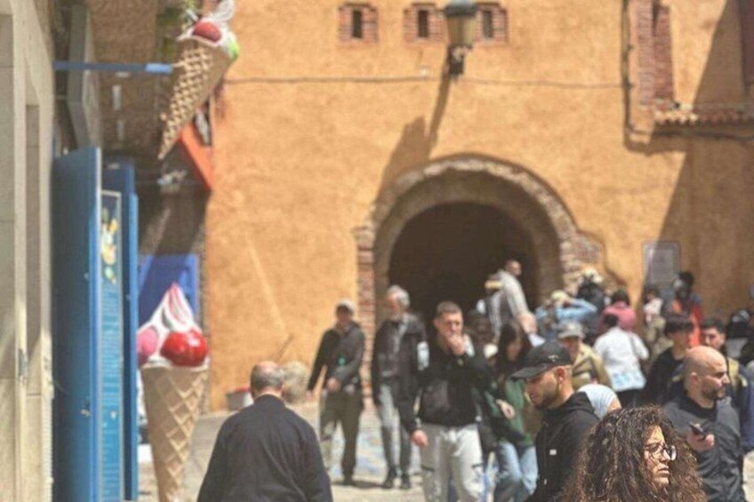 A crowded street with people walking, a building with an arched entrance, and a blue sign with red decorations. 3