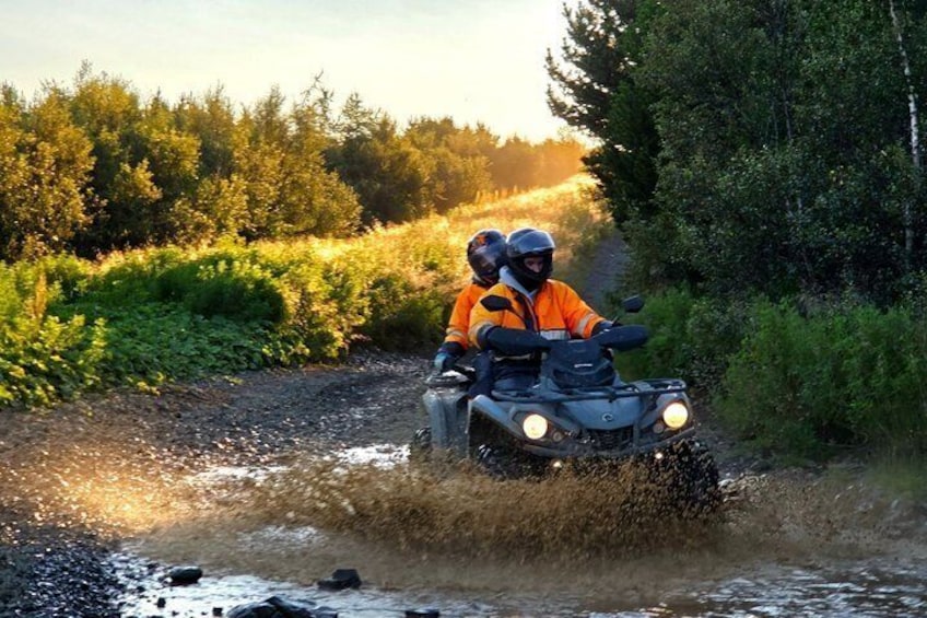 Two people on a quad bike crossing a shallow water body. 1