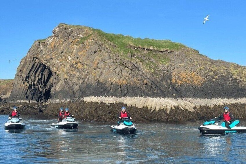 Four jet skis on calm water with a rocky cliff in the background. 3
