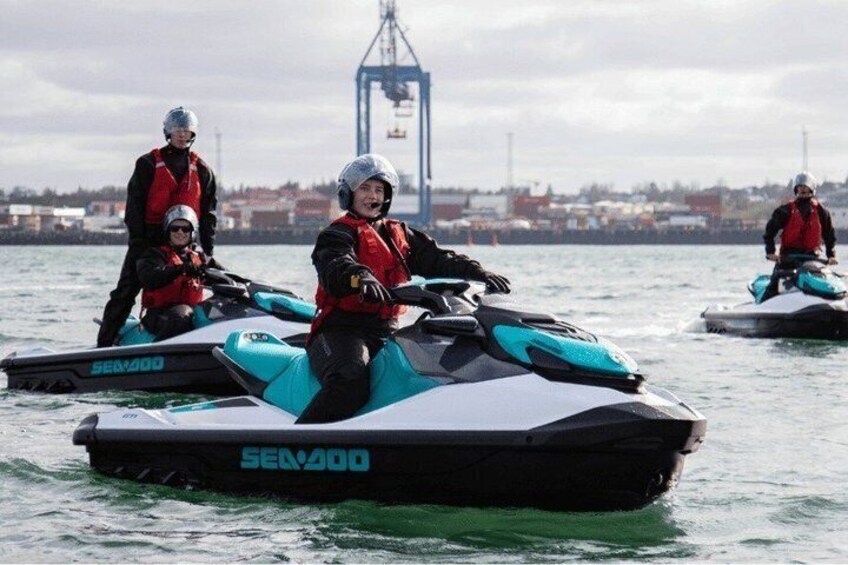 Three individuals on jet skis in a body of water with a bridge and buildings in the background. 5