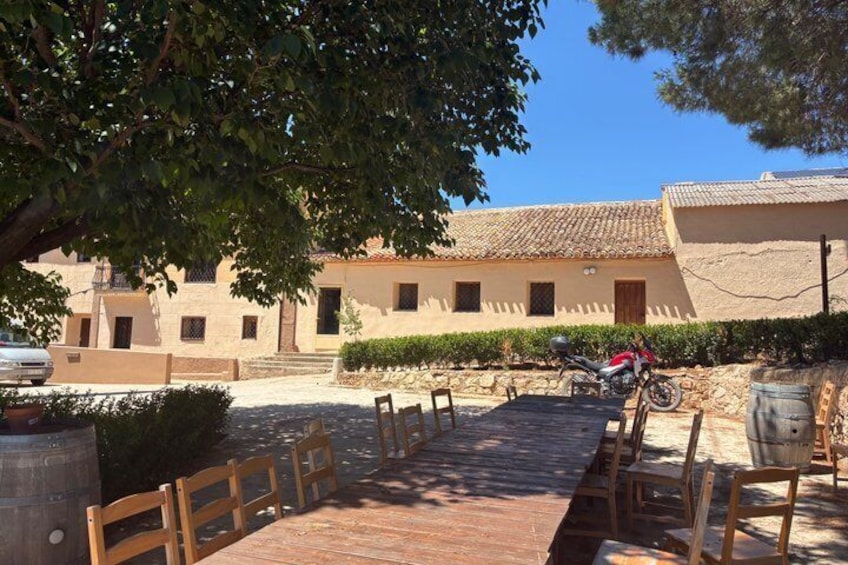 A long wooden table with chairs, a motorcycle, and a building with a tiled roof. 1