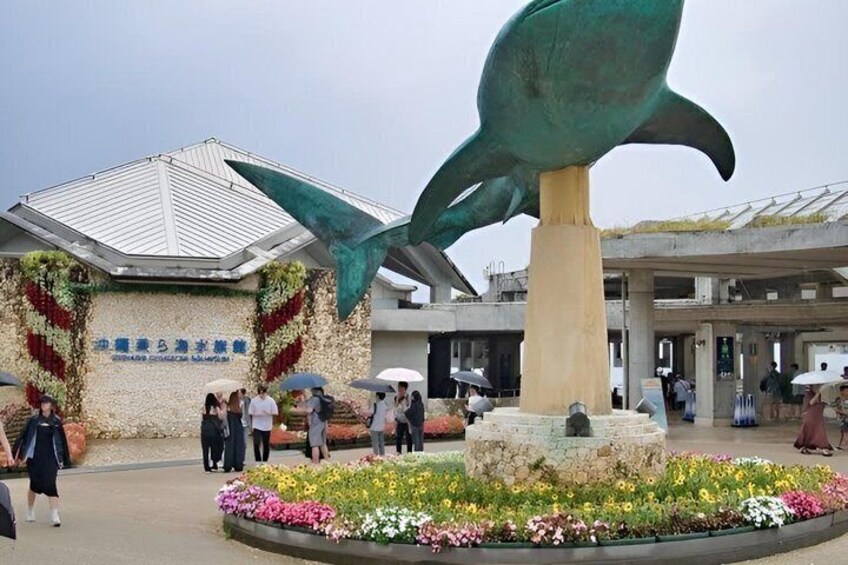 A public space with a large sculpture, a building with a tiled roof, and a flower bed. 3