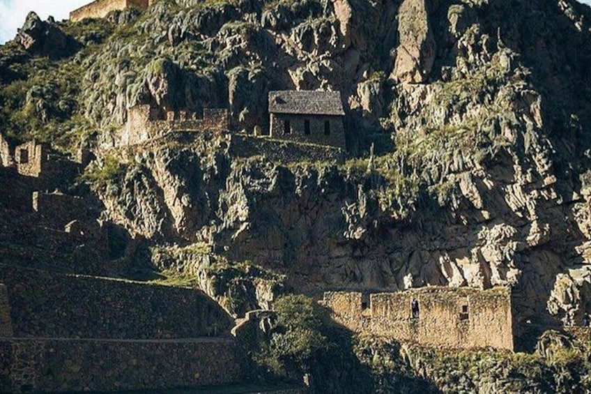 A fortress on a rocky hill with a small building on top and a fortified wall below. 5